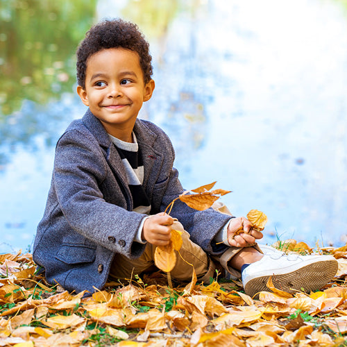 Preschool boy wearing fall clothing sitting down smiling. 